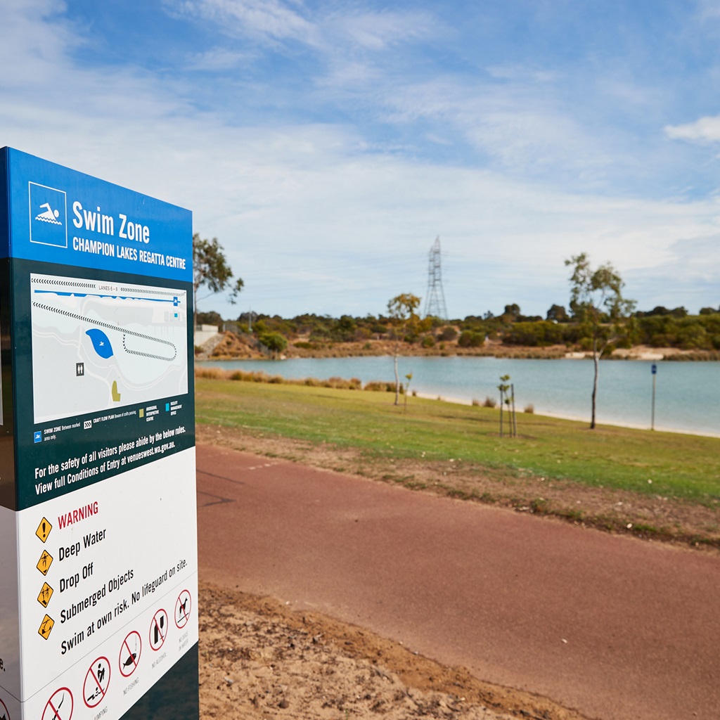 A photo of a swim zone sign on a path with the lake in the background at the Champion Lakes Regatta Centre in Champion Lakes, Perth